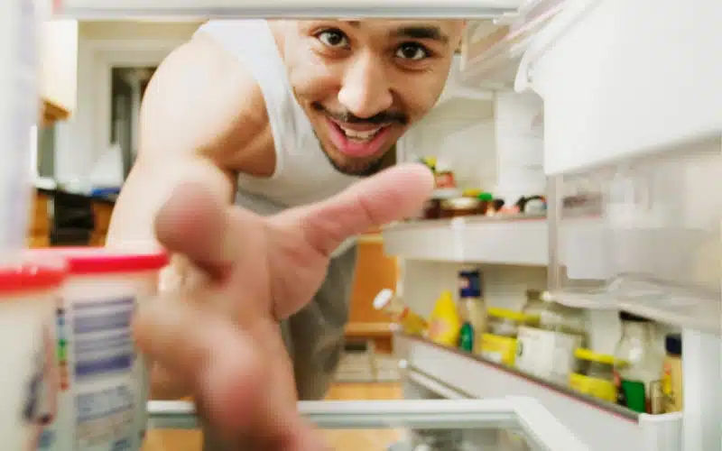 10 Refrigerator Repair Signs You Shouldn't Ignore 1 A smiling man, viewed from inside a refrigerator, reaches out towards the camera.