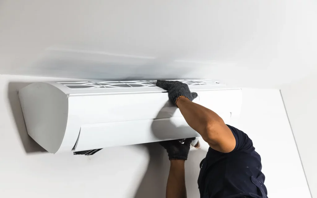 Air Conditioner Replacement Guide 1 A worker installs a white indoor air conditioning unit on a white wall.