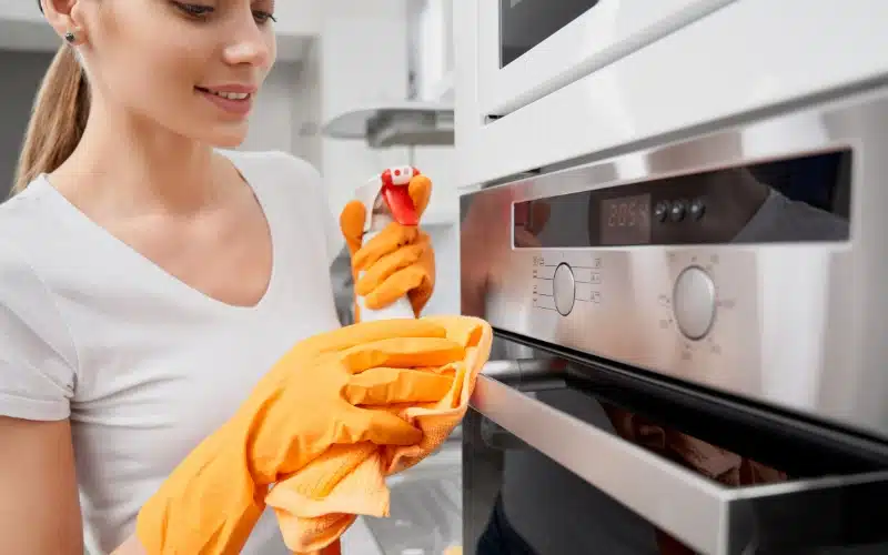 How to Extend the Lifespan of Oven 1 Wipes down a modern oven with a spray and cloth, embodying diligent oven care.