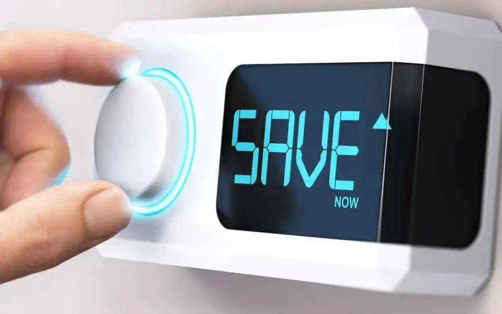 Save Money on Heating and Cooling: 6 Effective Tips 1 A hand turns a modern smart thermostat knob, featuring a blue glowing ring, with "SAVE NOW" displayed on its screen, suggesting energy savings.