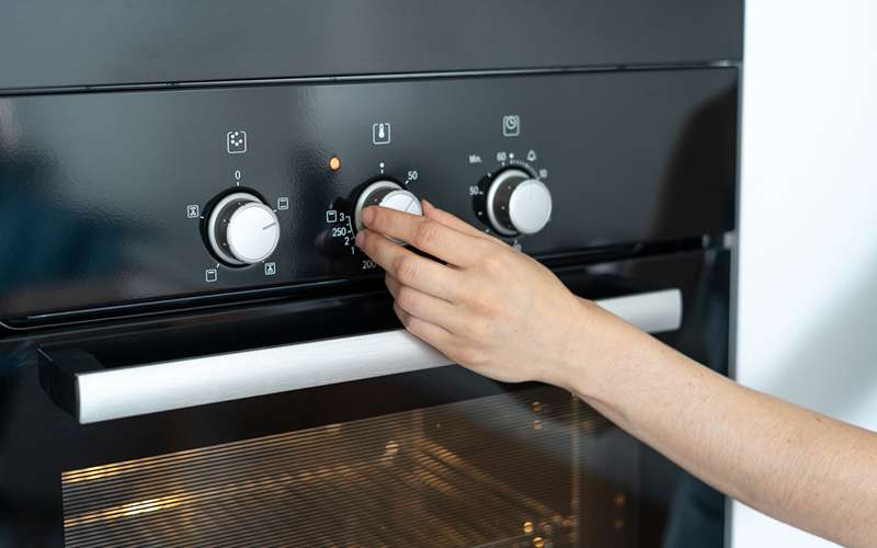 Woman select program turning switch at modern built in oven